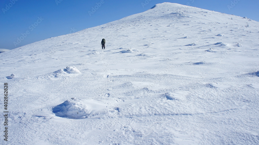 a lonely man climbs a snow-capped peak, on a winter cloudless frosty day