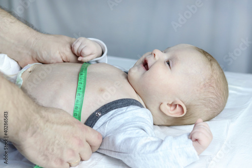 A specialist pediatrician measures the baby's body with a tape measure during a screening examination, side view. Copy space - concept of child health and disease prevention, pediatrics, growth