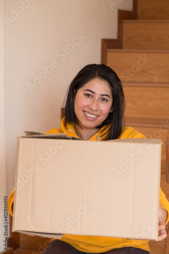 beautiful latin woman in her new apartment sitting with a cardboard box next to some wooden bleachers on a summer day