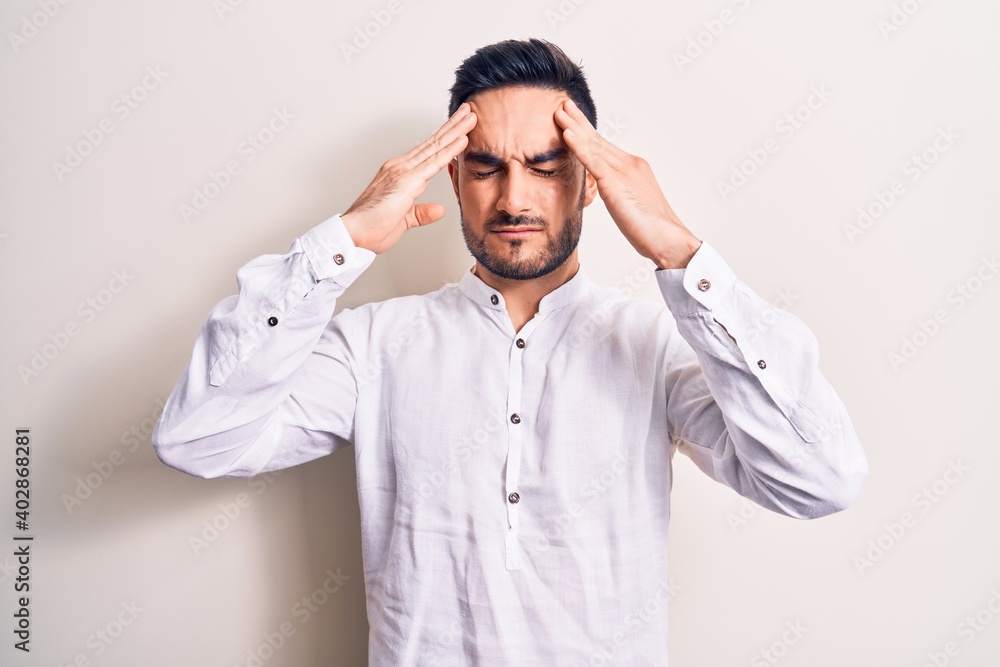 Young handsome man with beard wearing casual t-shirt standing over white background with hand on head, headache because stress. Suffering migraine. Young handsome man with beard wearing casual t-shirt standing over white background with hand on head, headache because stress. Suffering migraine.