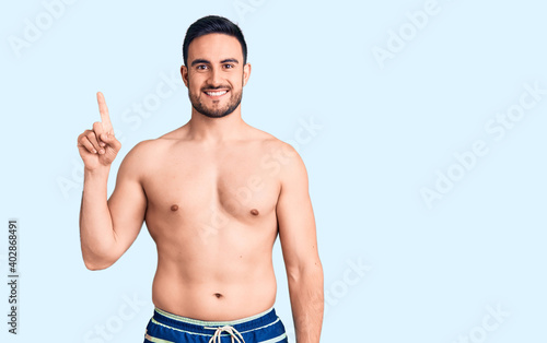 Young handsome man wearing swimwear showing and pointing up with finger number one while smiling confident and happy. © Krakenimages.com