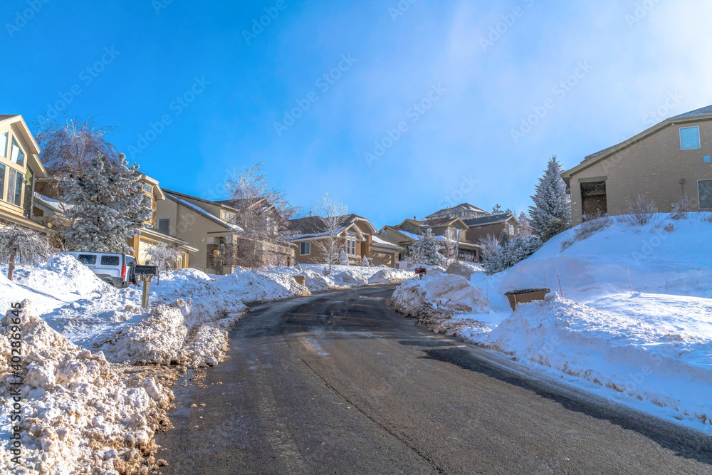 Road along homes with snowy yards against blue sky on a scenic winter landscape