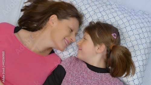 young mom and her daughter are cuddled and tickled on the bed at home