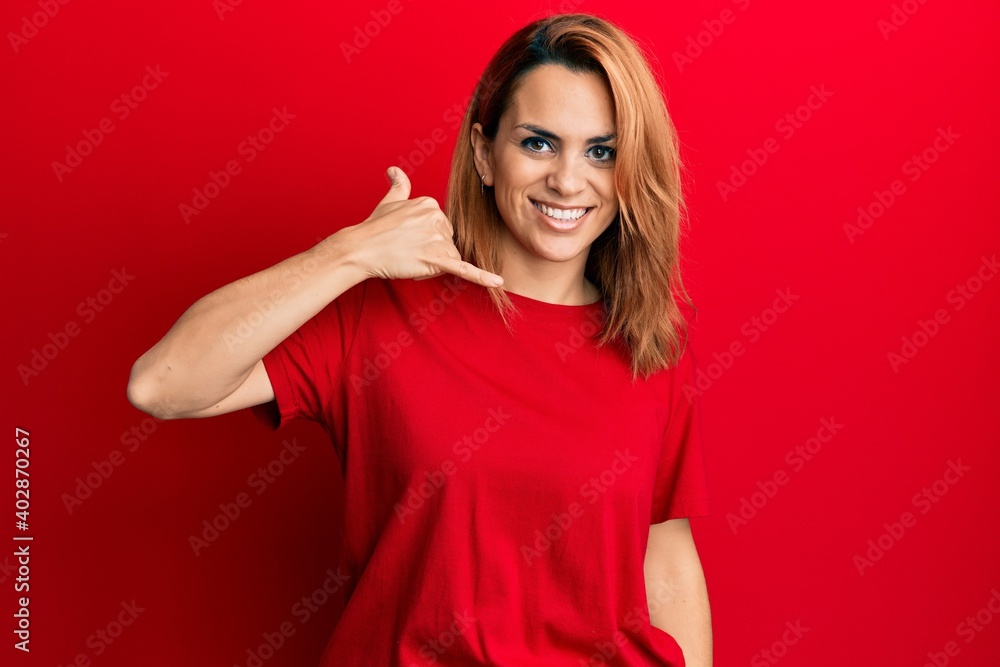 Hispanic young woman wearing casual red t shirt smiling doing phone gesture with hand and fingers like talking on the telephone. communicating concepts. Hispanic young woman wearing casual red t shirt smiling doing phone gesture with hand and fingers like talking on the telephone. communicating concepts.