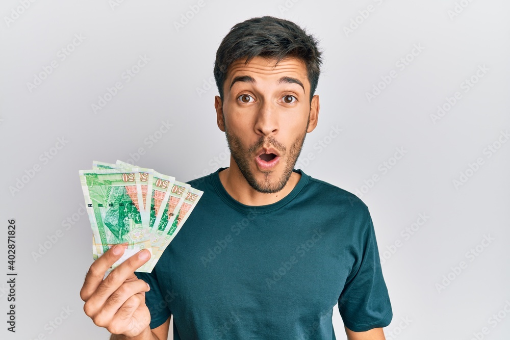 Young handsome man holding 50 hong kong dollars banknotes scared and amazed with open mouth for surprise, disbelief face Young handsome man holding 50 hong kong dollars banknotes scared and amazed with open mouth for surprise, disbelief face