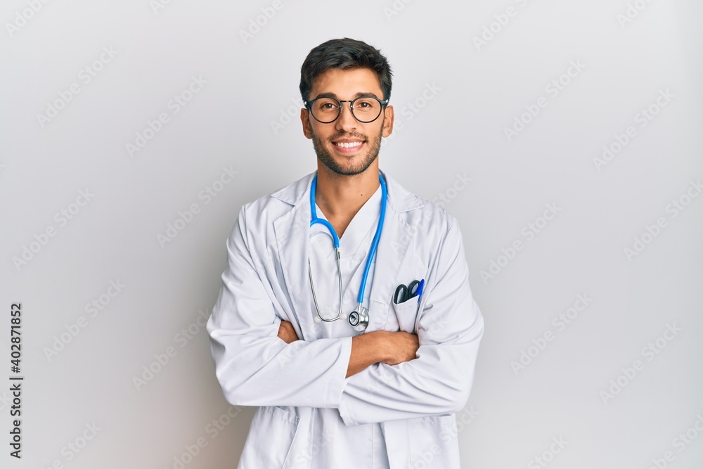 Young handsome man wearing doctor uniform and stethoscope happy face smiling with crossed arms looking at the camera. positive person. Young handsome man wearing doctor uniform and stethoscope happy face smiling with crossed arms looking at the camera. positive person.