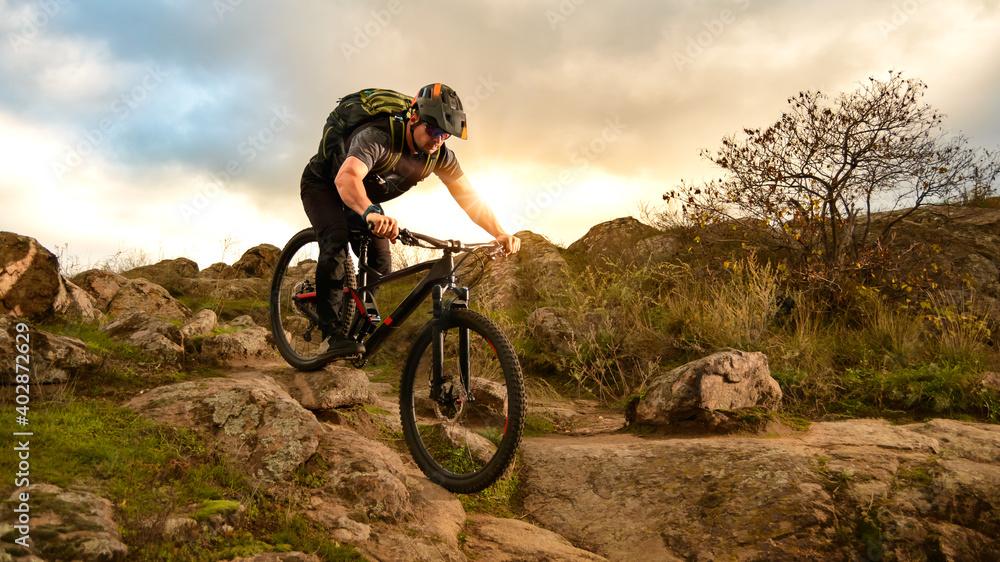 Naklejka premium Professional Cyclist Riding Bike on the Autumn Rocky Trail at Sunset. Extreme Sport and Enduro Biking Concept.
