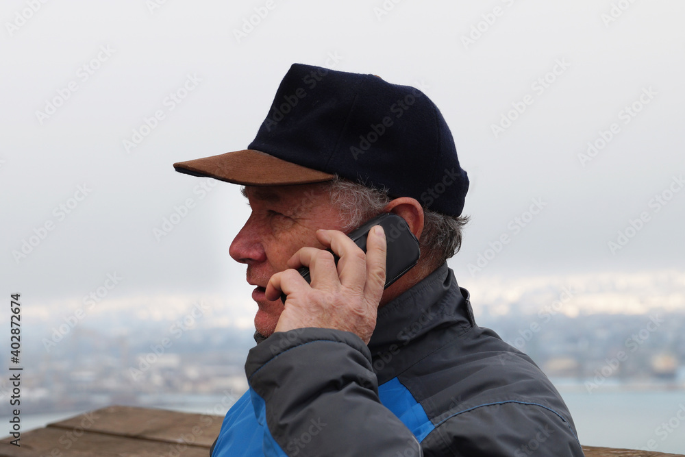 portrait of a middle-aged man talking on the phone in a cap on a natural background