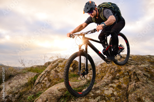Professional Cyclist Riding Bike on the Autumn Rocky Trail at Sunset. Extreme Sport and Enduro Biking Concept.