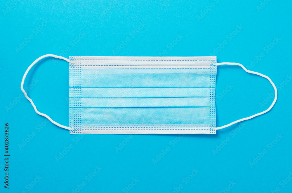 Mask on blue background. Surgical mask with rubber ear straps. Typical 3-ply surgical mask to cover the mouth and nose. Procedure mask from bacteria. Protection concept. Mask on blue background. Surgical mask with rubber ear straps. Typical 3-ply surgical mask to cover the mouth and nose. Procedure mask from bacteria. Protection concept.