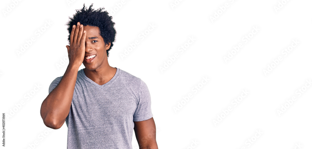 Handsome african american man with afro hair wearing casual clothes covering one eye with hand, confident smile on face and surprise emotion. Handsome african american man with afro hair wearing casual clothes covering one eye with hand, confident smile on face and surprise emotion.