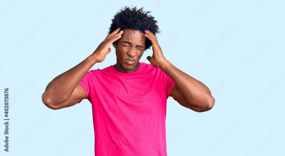 Handsome african american man with afro hair wearing casual pink tshirt suffering from headache desperate and stressed because pain and migraine. hands on head. Handsome african american man with afro hair wearing casual pink tshirt suffering from headache desperate and stressed because pain and migraine. hands on head.