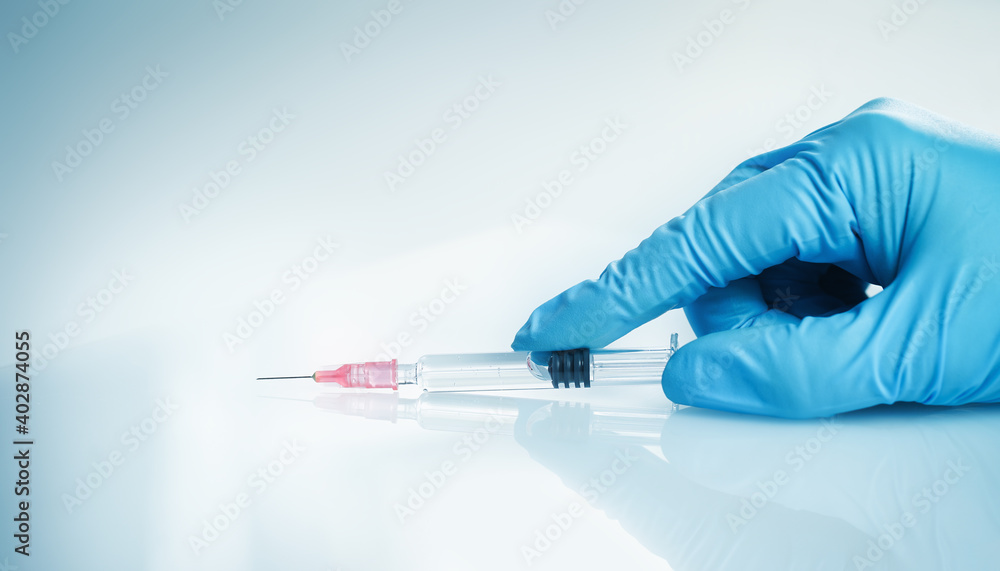 Doctor's hand with glass syringe with a needle on blue. copy space. Medication safe consumption and treatment, vaccine and immunization. Health and pharmacy and vaccination concept banner Doctor's hand with glass syringe with a needle on blue. copy space. Medication safe consumption and treatment, vaccine and immunization. Health and pharmacy and vaccination concept banner