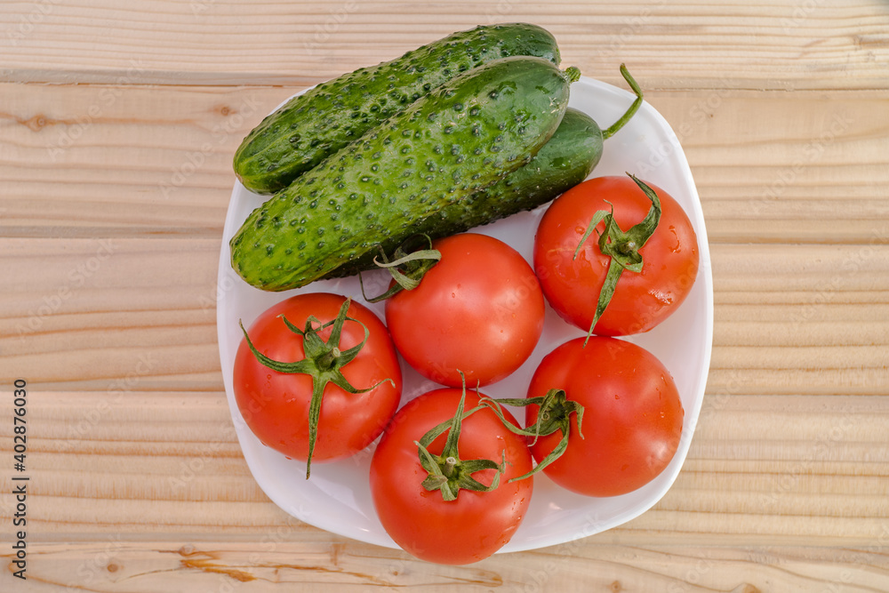 white plate top view of fresh vegetables from the garden such as tomatoes and cucumbers on a wooden table. white plate top view of fresh vegetables from the garden such as tomatoes and cucumbers on a wooden table.