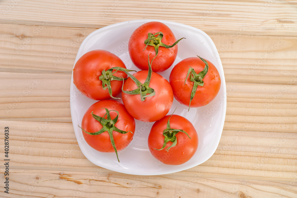 red tomatoes in a white plate on a wooden table top view. red tomatoes in a white plate on a wooden table top view.