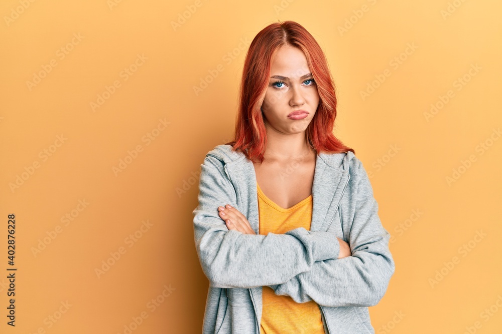 Young beautiful redhead woman wearing casual sporty sweatshirt skeptic and nervous, disapproving expression on face with crossed arms. negative person. Young beautiful redhead woman wearing casual sporty sweatshirt skeptic and nervous, disapproving expression on face with crossed arms. negative person.