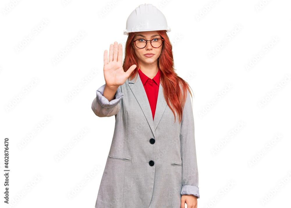 Young redhead woman wearing architect hardhat doing stop sing with palm of the hand. warning expression with negative and serious gesture on the face.