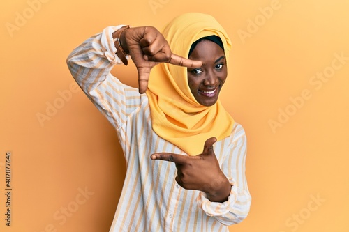 Beautiful african young woman wearing traditional islamic hijab scarf smiling making frame with hands and fingers with happy face. creativity and photography concept.