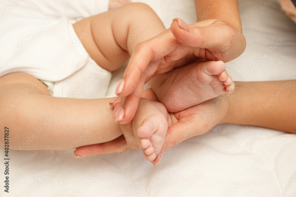 Hands of woman holds baby foot, blurred background Hands of woman holds baby foot, blurred background