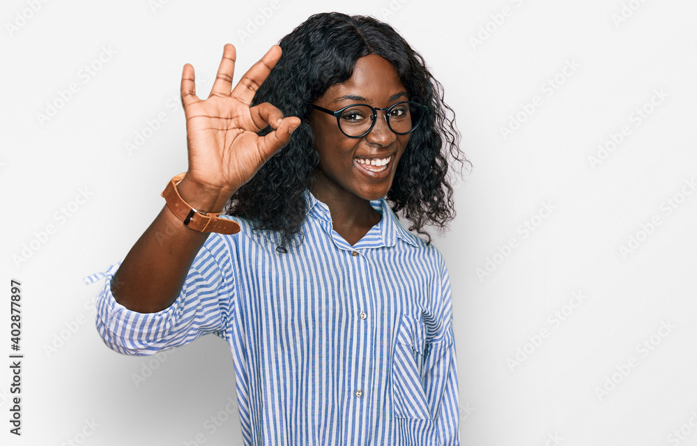 Beautiful african young woman wearing casual clothes and glasses smiling positive doing ok sign with hand and fingers. successful expression. Beautiful african young woman wearing casual clothes and glasses smiling positive doing ok sign with hand and fingers. successful expression.