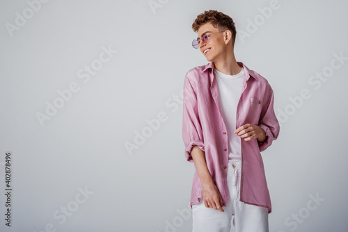 Young fashionable happy smiling man wearing trendy sunglasses, pink, lilac silk shirt, white t-shirt, trousers. Summer fashion conception, studio portrait. Copy, empty space for text