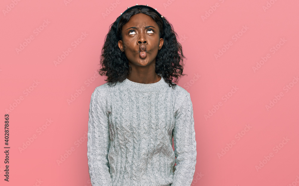 Beautiful african young woman wearing casual winter sweater making fish face with lips, crazy and comical gesture. funny expression. Beautiful african young woman wearing casual winter sweater making fish face with lips, crazy and comical gesture. funny expression.