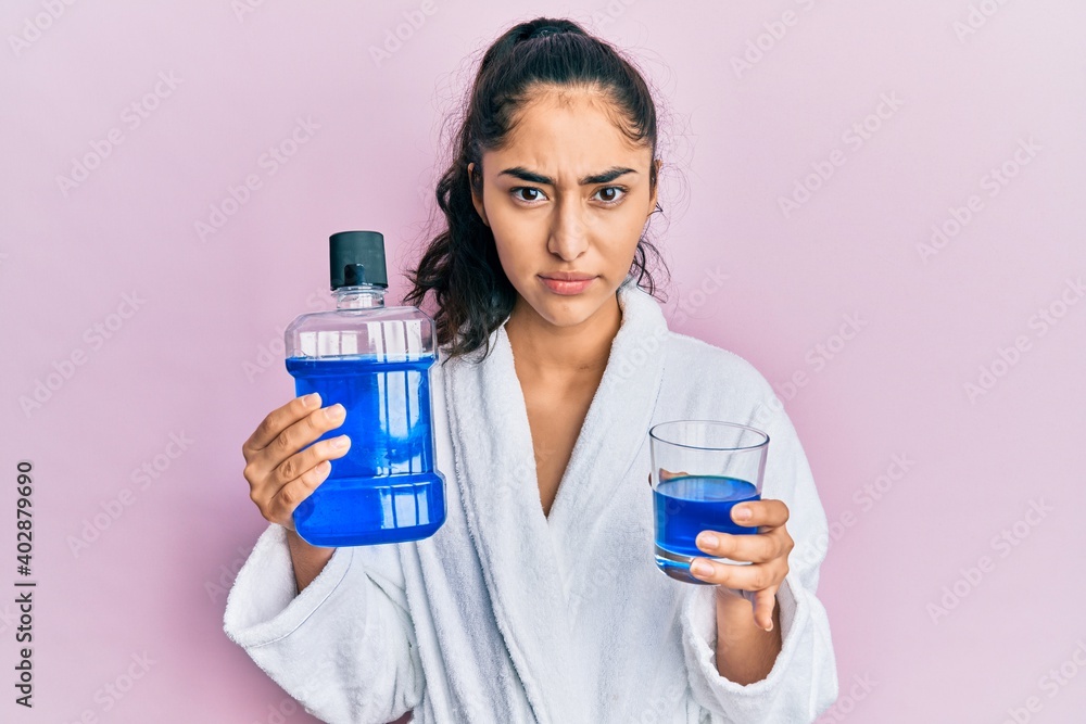 Hispanic teenager girl with dental braces holding mouthwash skeptic and nervous, frowning upset because of problem. negative person. Hispanic teenager girl with dental braces holding mouthwash skeptic and nervous, frowning upset because of problem. negative person.