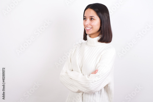 Young brunette woman wearing white knitted sweater against white background cross hands look copy space