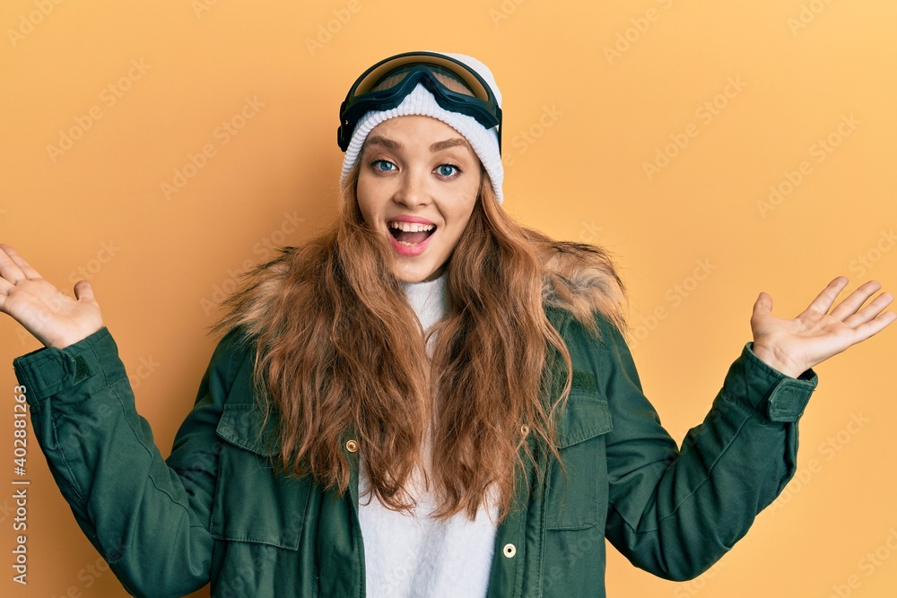 Beautiful blonde caucasian woman wearing snow wear and sky glasses celebrating victory with happy smile and winner expression with raised hands Beautiful blonde caucasian woman wearing snow wear and sky glasses celebrating victory with happy smile and winner expression with raised hands
