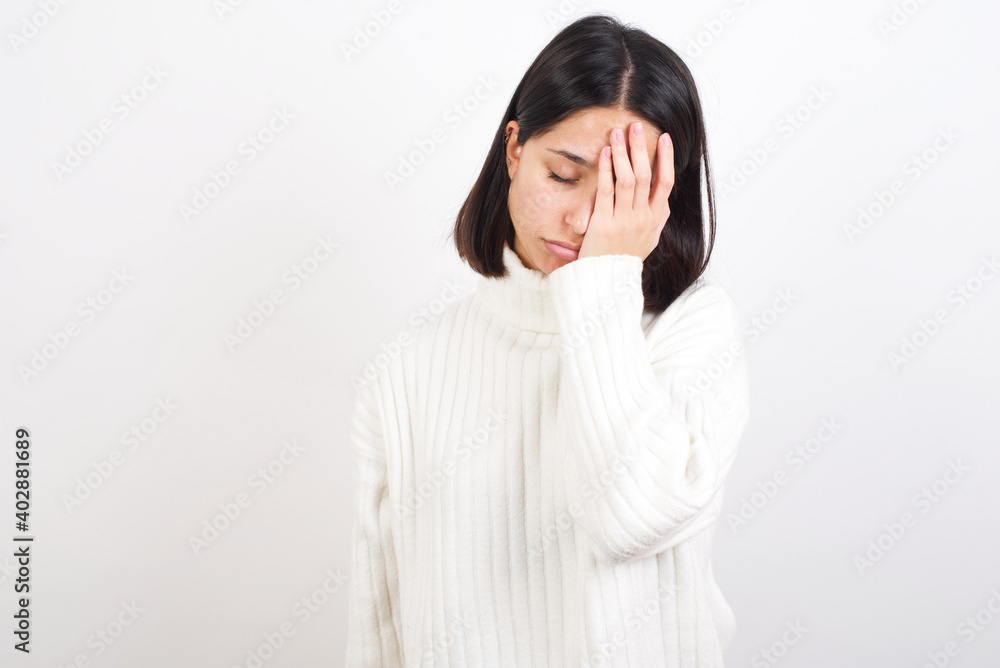 Tired overworked Young brunette woman wearing white knitted sweater has sleepy expression, gloomy look, covers face with hand, has eyes shut, gasps from tiredness, fatigue after party Tired overworked Young brunette woman wearing white knitted sweater has sleepy expression, gloomy look, covers face with hand, has eyes shut, gasps from tiredness, fatigue after party