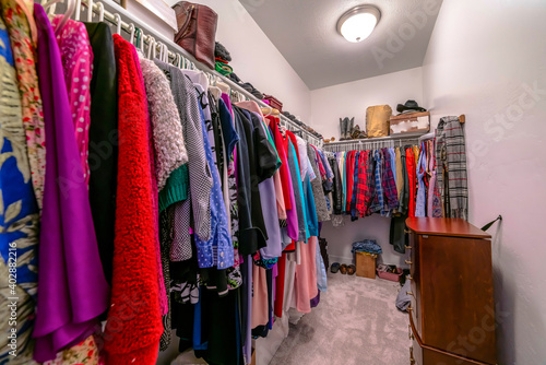 Walk in closet interior with colorful clothes hanging on rods against white wall