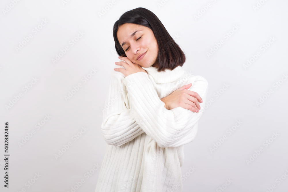 Young brunette woman wearing white knitted sweater against white background Hugging oneself happy and positive, smiling confident. Self love and self care Young brunette woman wearing white knitted sweater against white background Hugging oneself happy and positive, smiling confident. Self love and self care