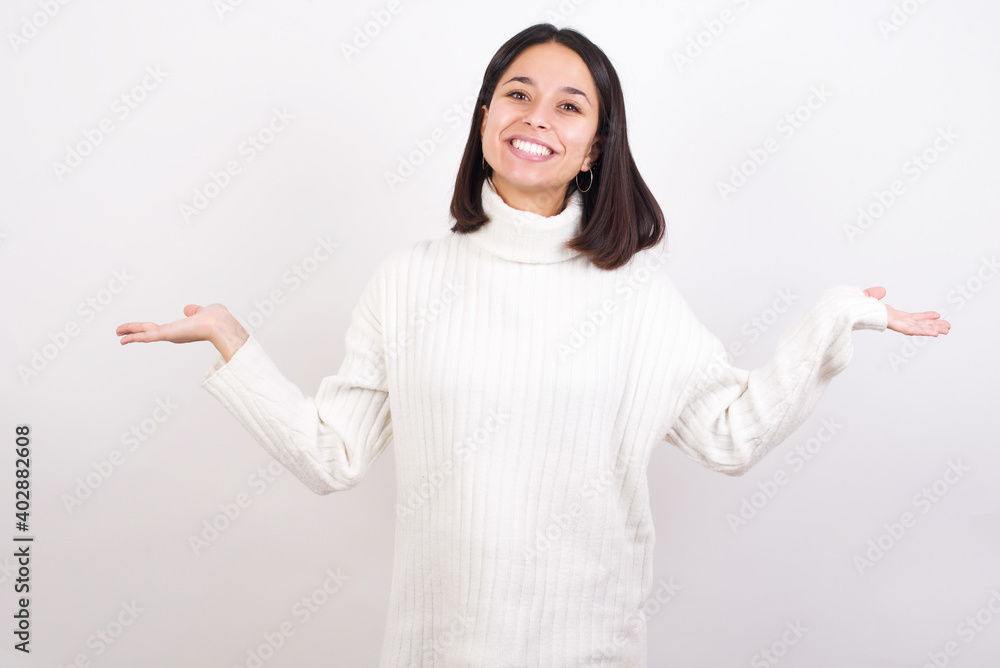 Cheerful cheery optimistic Young brunette woman wearing white knitted sweater against white background holding two palms copy space Cheerful cheery optimistic Young brunette woman wearing white knitted sweater against white background holding two palms copy space