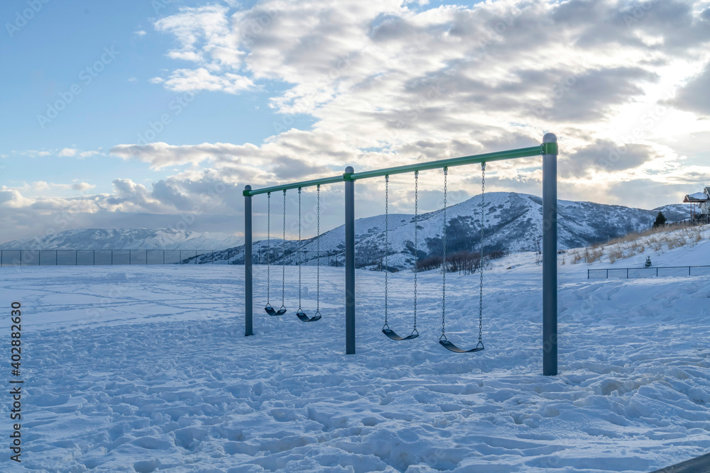 Playground swing with thick snow on ground and views of mountain and cloudy sky Playground swing with thick snow on ground and views of mountain and cloudy sky