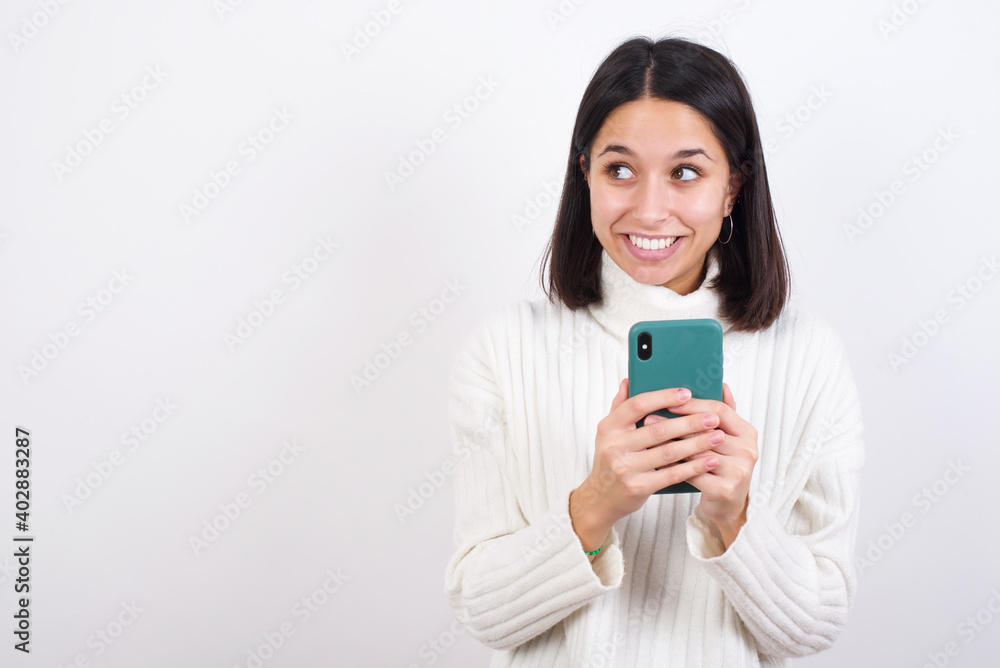 Young brunette woman wearing white knitted sweater against white background holding in hands showing new cell Young brunette woman wearing white knitted sweater against white background holding in hands showing new cell