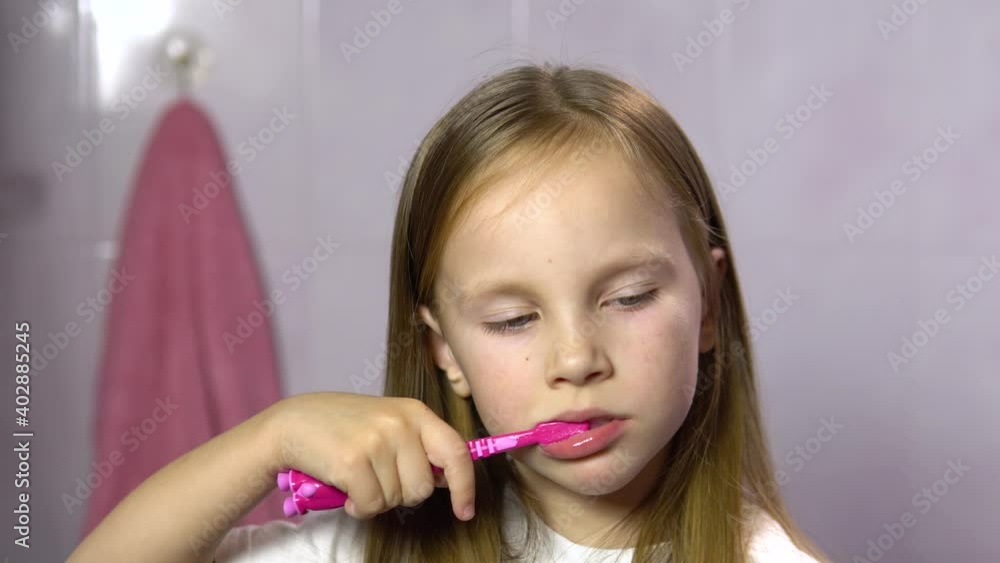 Little blonde girl brushes her teeth in the bathroom.Close-up.A 4-5 year old girl is brushing her teeth with a pink toothbrush. Little blonde girl brushes her teeth in the bathroom.Close-up.A 4-5 year old girl is brushing her teeth with a pink toothbrush.