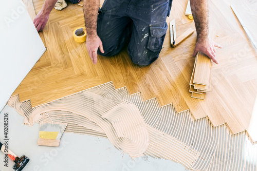 worker installing oak herringbone parquet floor during home improvement