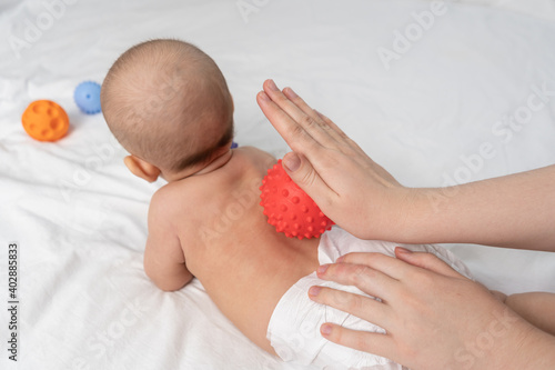 Doctor hands massage newborn with red rubber ball