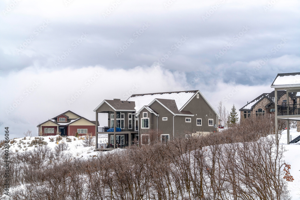 Homes on hill top covered with snow in winter against background of cloudy sky Homes on hill top covered with snow in winter against background of cloudy sky