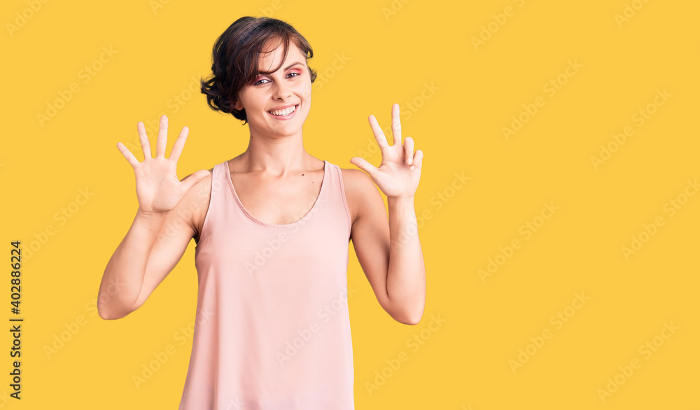 Beautiful young woman with short hair wearing casual style with sleeveless shirt showing and pointing up with fingers number eight while smiling confident and happy. Beautiful young woman with short hair wearing casual style with sleeveless shirt showing and pointing up with fingers number eight while smiling confident and happy.
