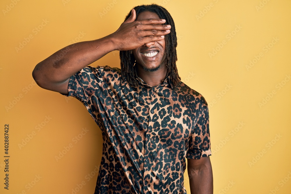 African american man with braids wearing leopard animal print shirt smiling and laughing with hand on face covering eyes for surprise. blind concept. African american man with braids wearing leopard animal print shirt smiling and laughing with hand on face covering eyes for surprise. blind concept.