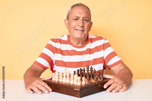 Senior handsome man with gray hair playing chess sitting on the table with a happy and cool smile on face. lucky person.