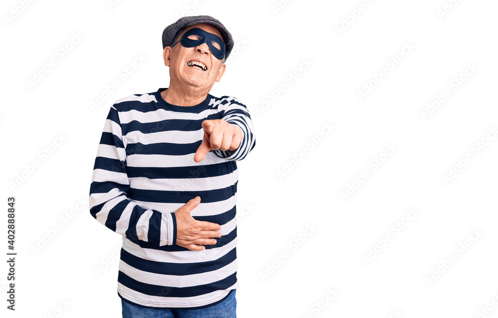 Senior handsome man wearing burglar mask and t-shirt laughing at you, pointing finger to the camera with hand over body, shame expression