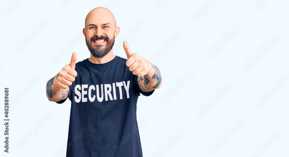 Fototapeta premium Young handsome man wearing security t shirt approving doing positive gesture with hand, thumbs up smiling and happy for success. winner gesture.