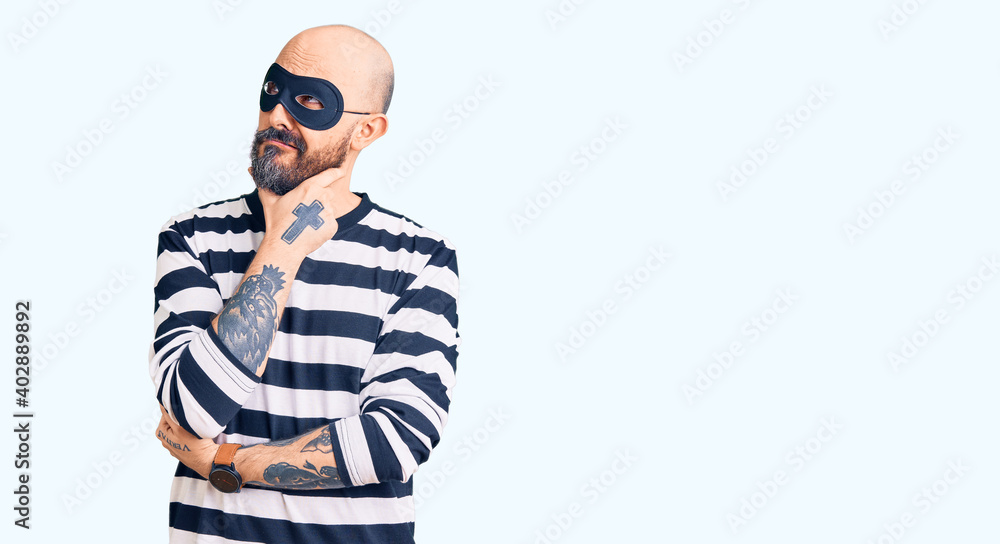 Young handsome man wearing burglar mask thinking worried about a question, concerned and nervous with hand on chin Young handsome man wearing burglar mask thinking worried about a question, concerned and nervous with hand on chin
