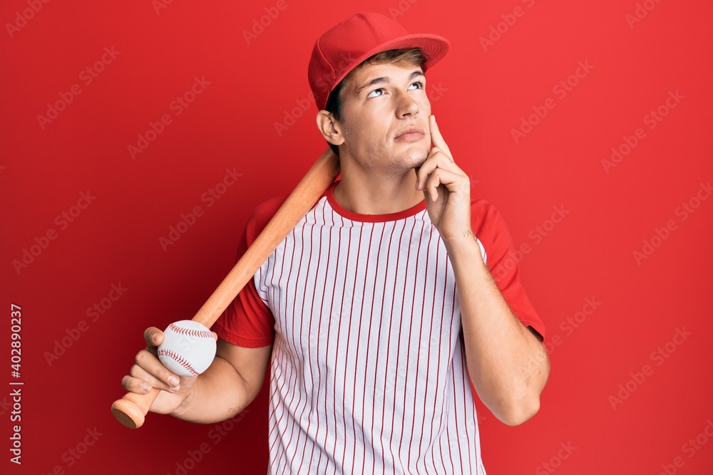 Handsome caucasian man playing baseball holding bat and ball serious face thinking about question with hand on chin, thoughtful about confusing idea