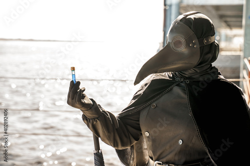 plague doctor in empty city on empty pier holds vaccine