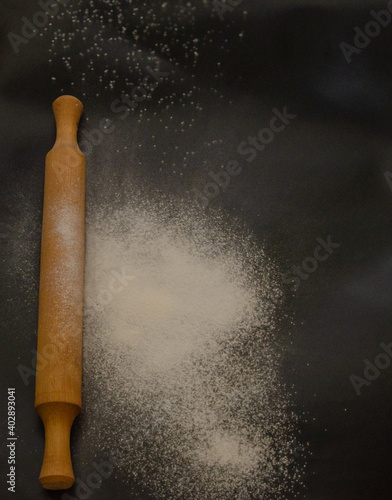 Rolling pin and white flour on a dark background. Cooking