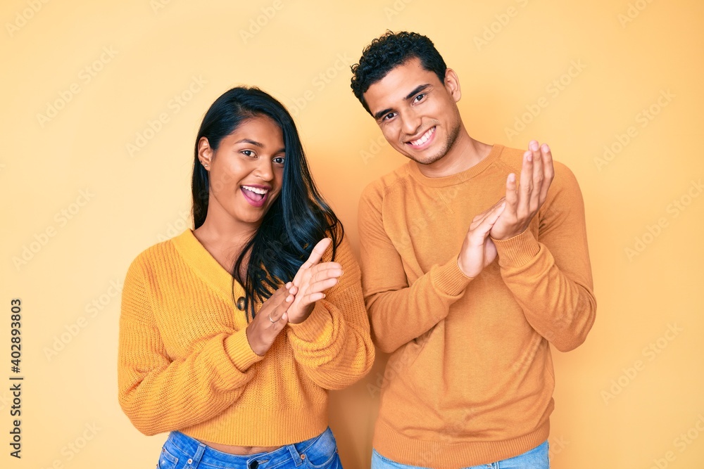 Beautiful latin young couple wearing casual clothes together clapping and applauding happy and joyful, smiling proud hands together Beautiful latin young couple wearing casual clothes together clapping and applauding happy and joyful, smiling proud hands together