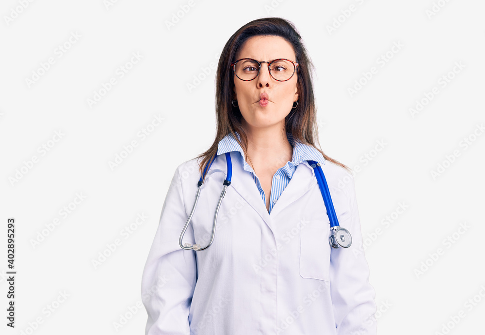 Fototapeta premium Young beautiful woman wearing doctor stethoscope and glasses making fish face with lips, crazy and comical gesture. funny expression.